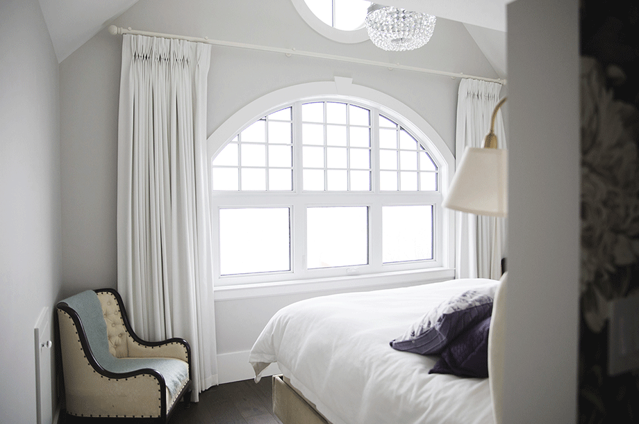 guest room with chair in the corner and large window with large drawn curtains