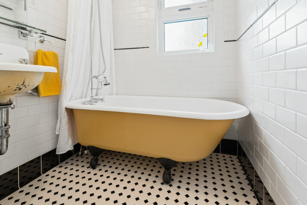 yellow stand alone clawfoot tub and black and white tiles