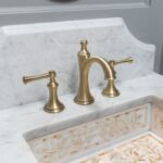 Exquisite bathroom remodel in a luxury Loudoun County home merging country, traditional and rustic styles. White sinks and opulent gold hardware add a touch of sophistication to this masterfully designed space, combining timeless charm with modern elegance.