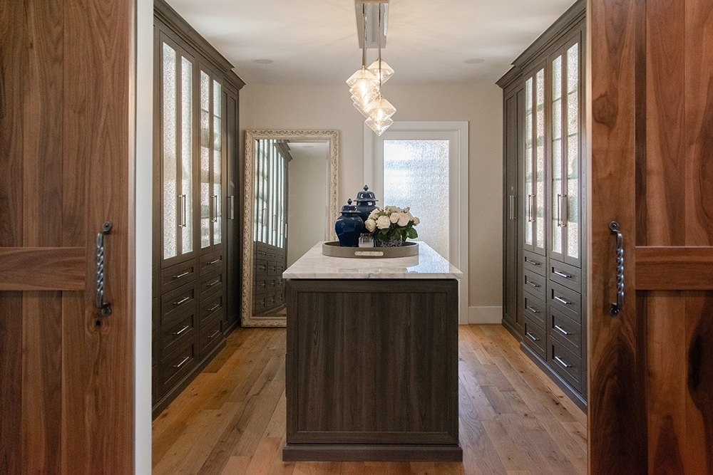 Master closet exudes luxury with a central island, impeccable lighting and rich floor wooding. Elevate your wardrobe experience with our rustic and traditional custom build and design in Loudoun County.