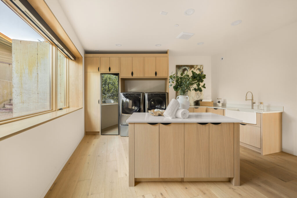a very spacious laundry room with an island, white oak custom cabinetry, utility sink and a large window | Lake Washington | Alair Homes Kirkland 