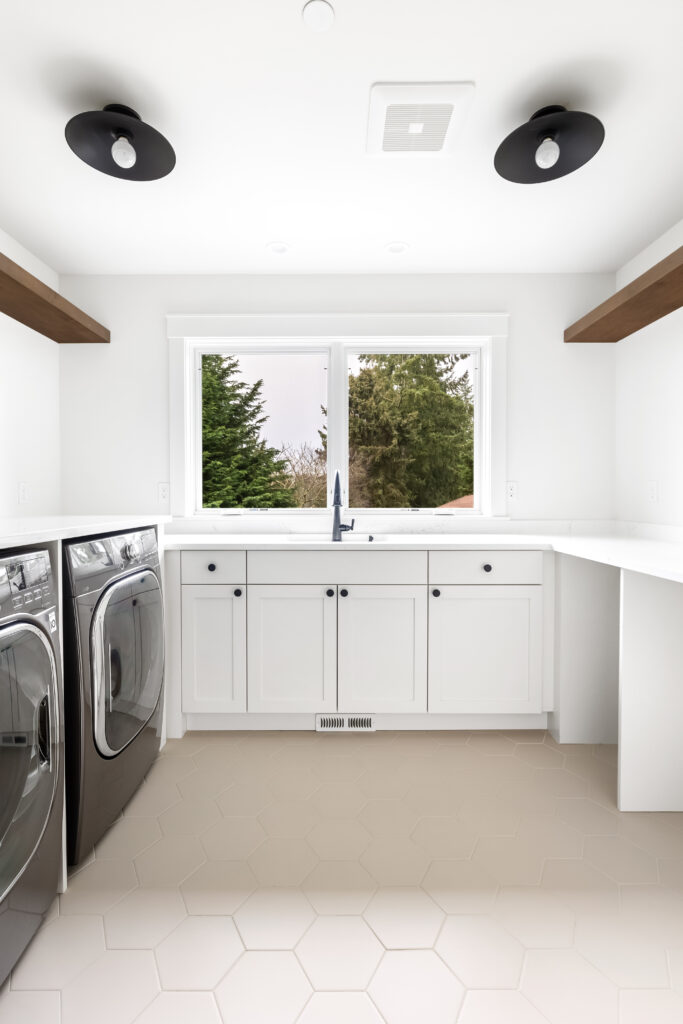 a custom laundry room with a pair of semi-flush mount lights, floating shelves, utility sink and plenty of countertop space | Lake Washington | Alair Homes Kirkland 