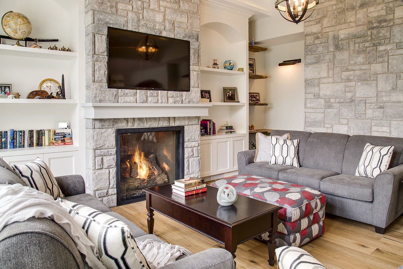 Cozy custom living space with burning stone fireplace built-in cabinetry and grey sofas