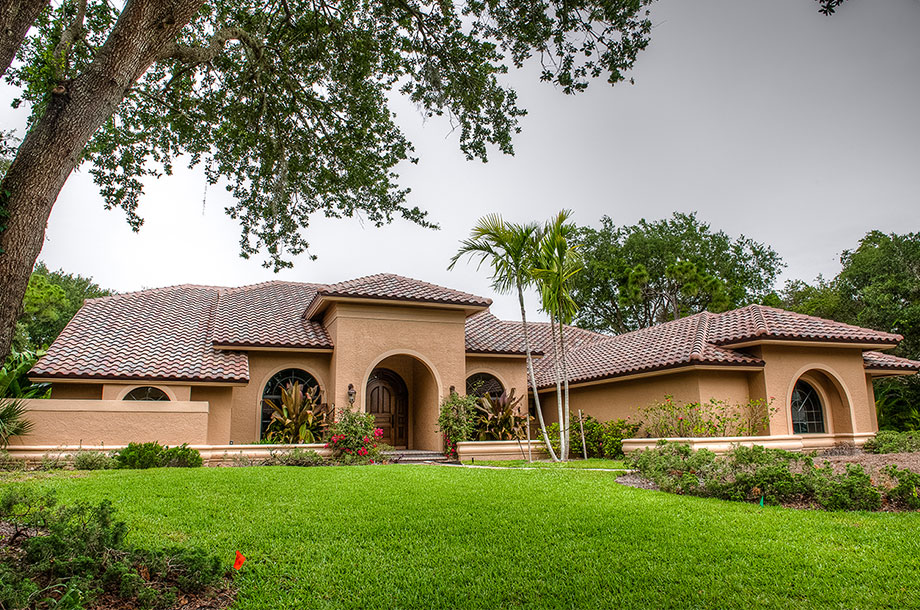 adobe style single story custom home surrounded by trees with healthy turfgrass front lawn