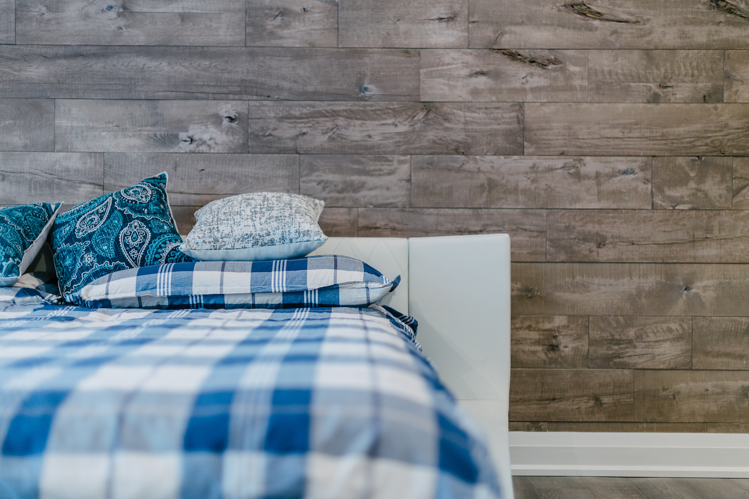 corner of bed with blue and white checkered comforter against wall with shiplap pattern