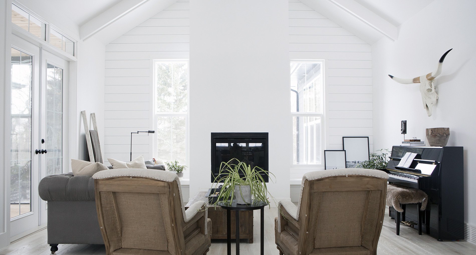 all white modern living space with two light leather recliners with skull hanging above small piano