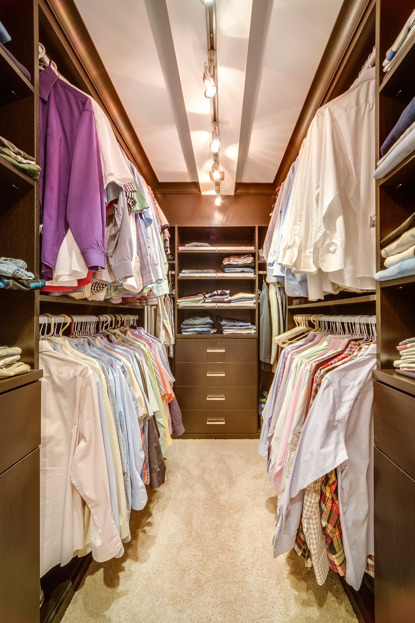 filled walk in closet with built in shelving and drawers and multilevel hangin rods