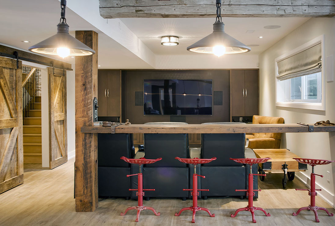 Custom basement entertainment studio with sliding wood barn doors and natural wood bar with red barstools