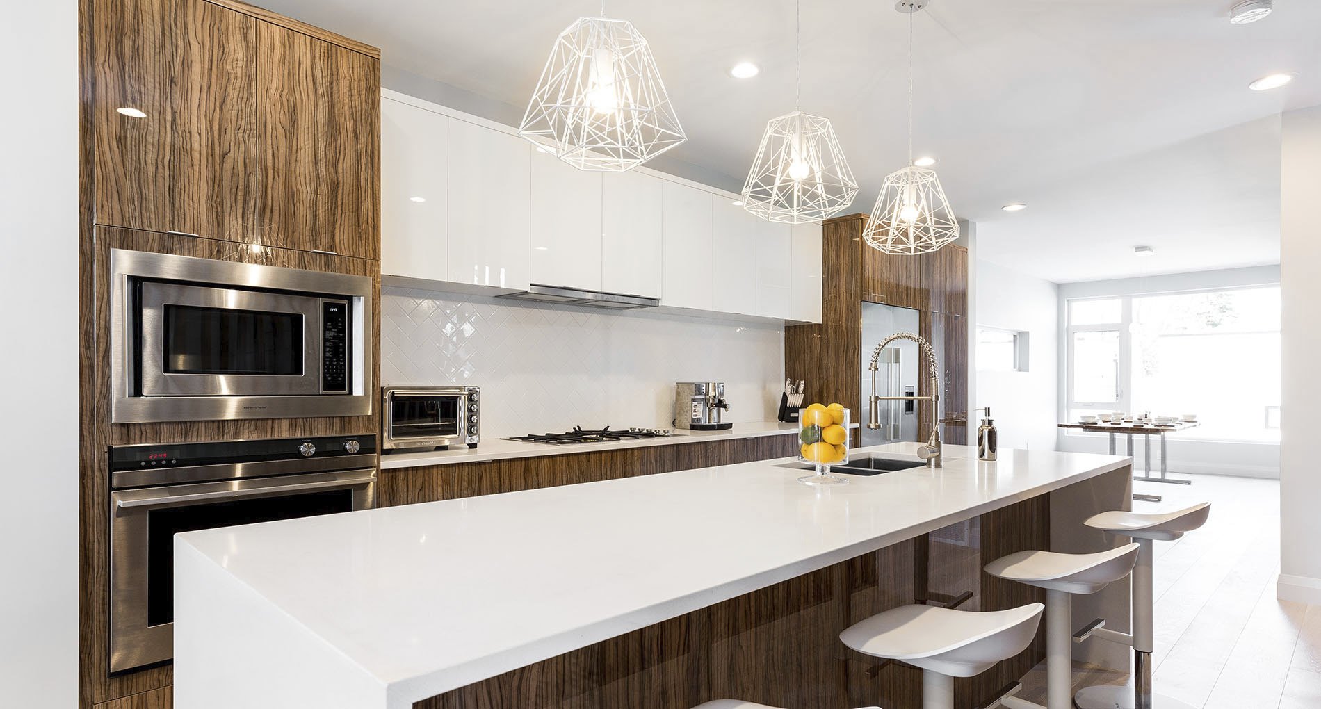 Kitchen with glossy white finishings and wood accents and custom white geometric overhead lighting fixtures.