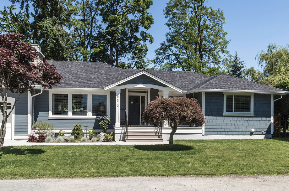 exterior of blue grey ranch style custom home with turfgrass lawn and small tree 