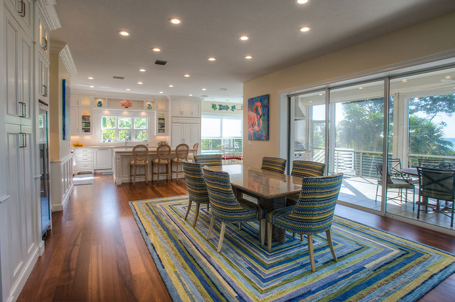 custom dining area open concept with kitchen in background surrounded by windows overlooking backyard