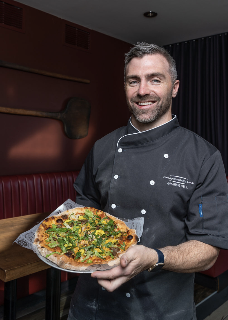 Alair Partner Graeme Bell holding custom pizza for charity