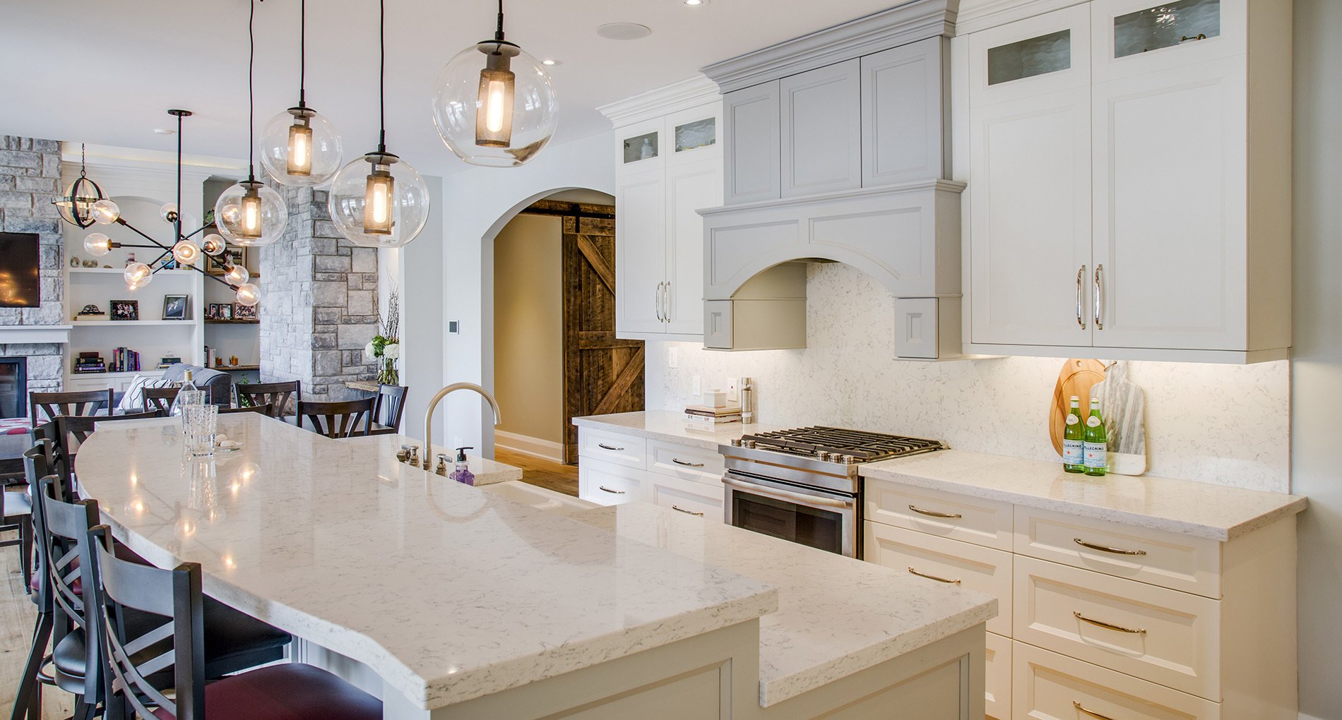 Custom kitchen with cream cabinetry and iron bar stools with leather cushions against long waved island