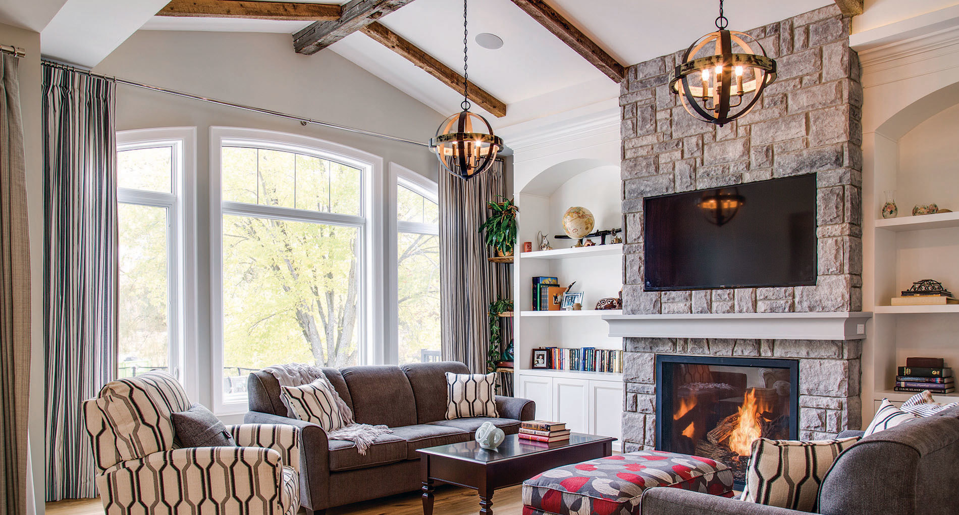 cozy living space with large window on one wall and stone fireplace and built in shelves on the other